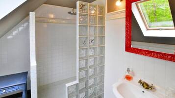 Une salle de bain avec une douche, un lavabo avec un miroir et une fenêtre donnant sur un espace verdoyant.