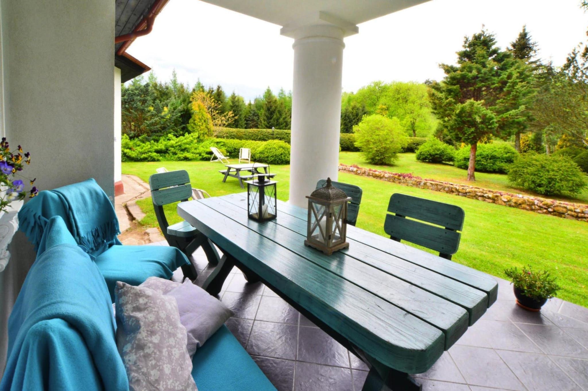 Un porche techado con una mesa y sillas de madera, un banco y vistas a un jardín cuidado.