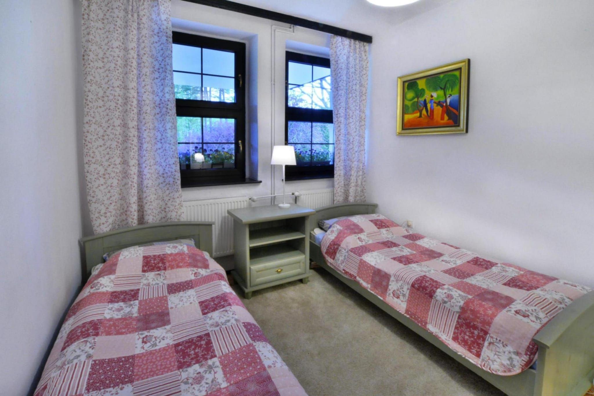 Une chambre avec deux lits simples, une table de chevet, une fenêtre avec des rideaux et un tableau au mur.