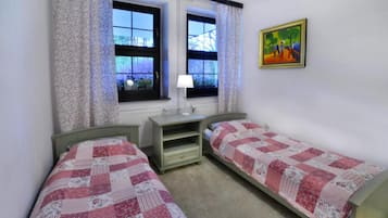 Une chambre avec deux lits simples, une table de chevet, une fenêtre avec des rideaux et un tableau au mur.