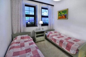 Une chambre avec deux lits simples, une table de chevet, une fenêtre avec des rideaux et un tableau au mur.