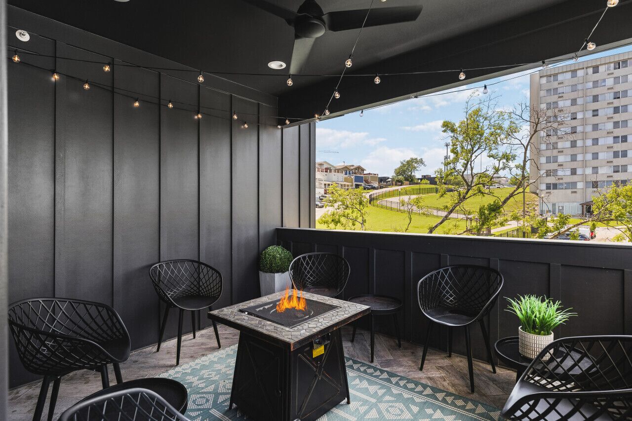 A balcony with a fire pit, black chairs, and a view of a residential area.