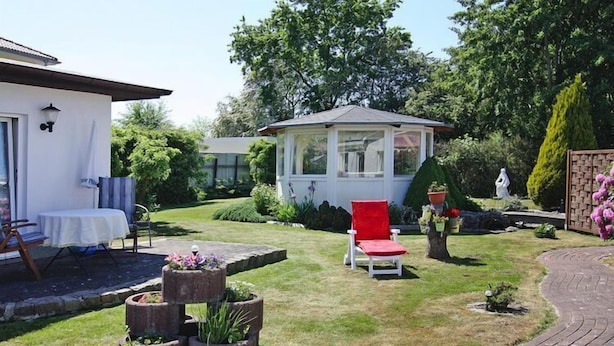 A garden with a gazebo, a red chair, and a white building with a covered patio. - Appartementhaus Nicole, Zinnowitz (Zinnowitz)