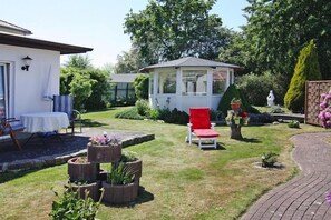 Un jardin agrémenté d’un belvédère, d’une chaise rouge et d’un bâtiment blanc doté d’un patio couvert.