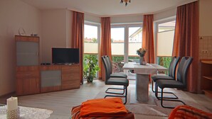 A modern living room with a TV, wooden cabinet, and a dining area with chairs and a table. - Appartementhaus Nicole, Zinnowitz (Zinnowitz)