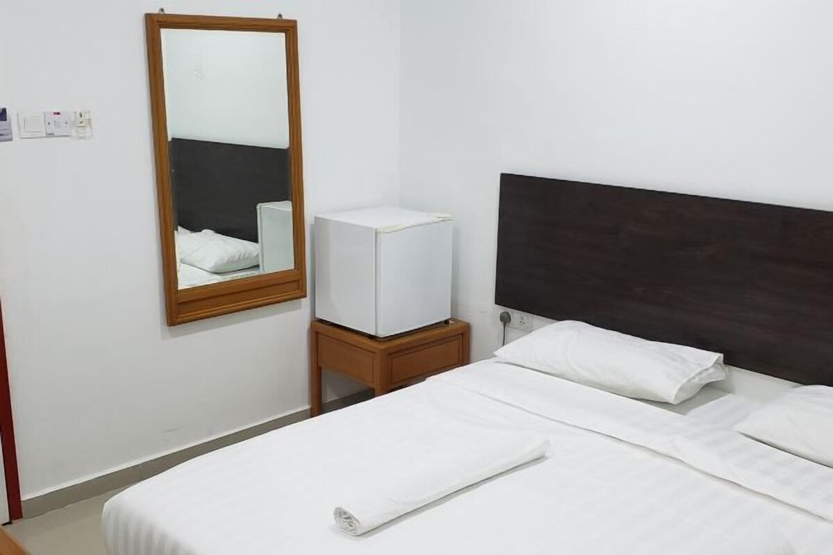 A hotel room with a bed, a wooden headboard, a small bedside table with a television, a mirror, and a white wall.