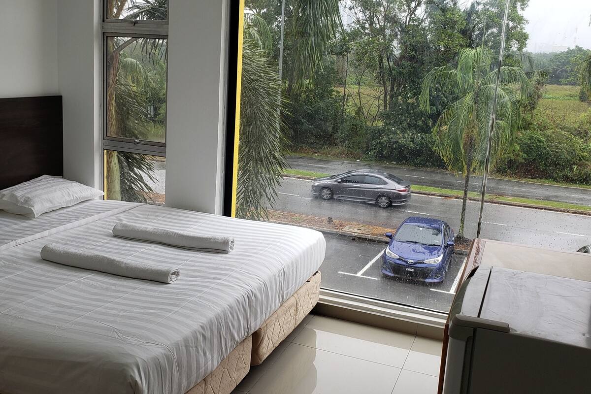 Un dormitorio con cama, almohadas y vistas a una calle con coches.