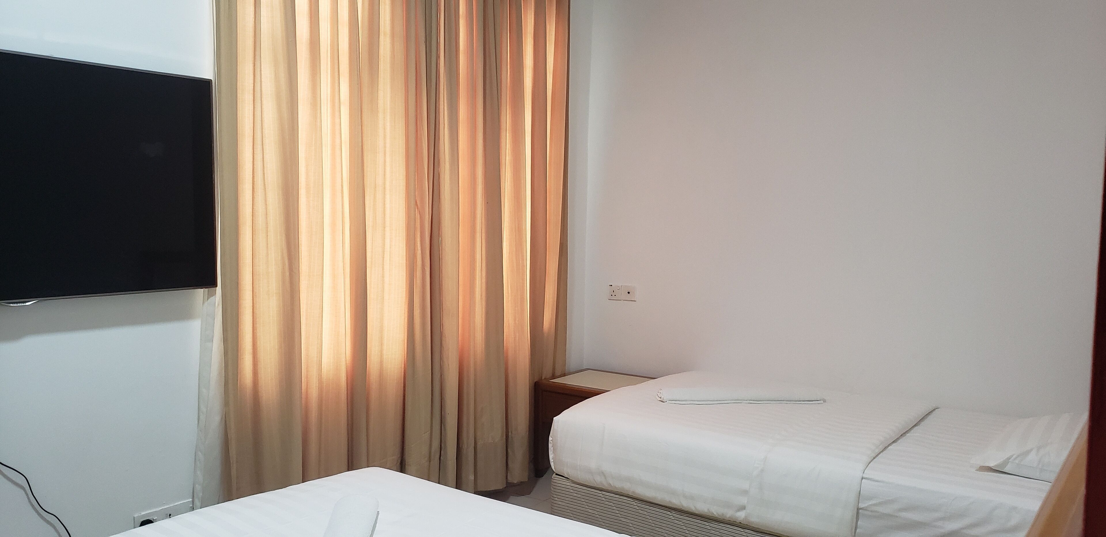 A small, simple room with a bed, a TV mounted on the wall, and a curtain.
