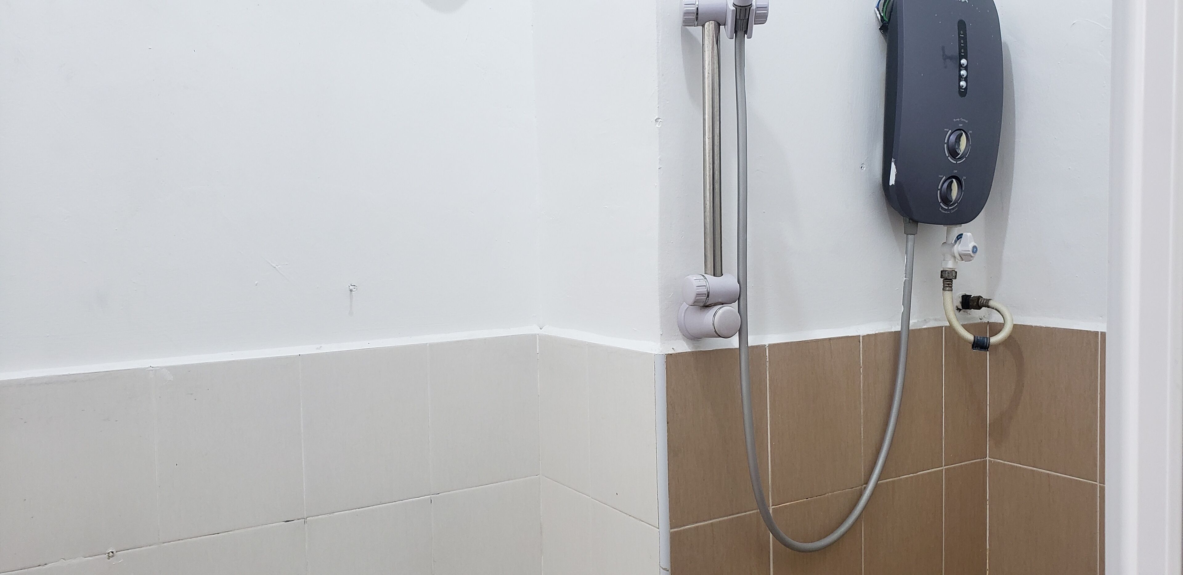 A shower area with a handheld showerhead and a wall-mounted control panel.