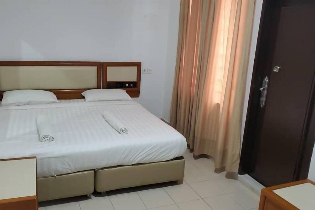 Una habitación de hotel con cama, dos mesitas de noche, un armario y un espejo.