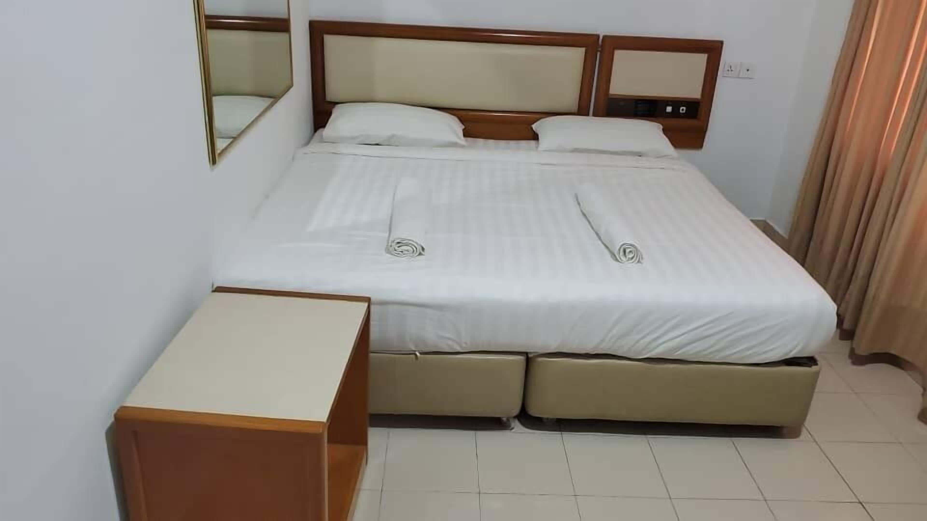 A neatly made bed with a headboard, a bedside table, and a small cabinet.