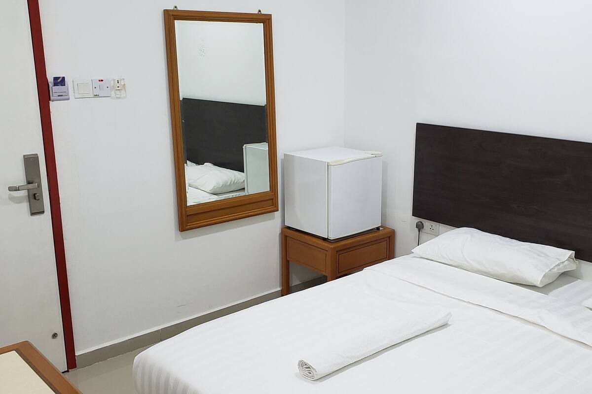 Una habitación de hotel con una cama individual, una mesita de noche, un espejo y un televisor.