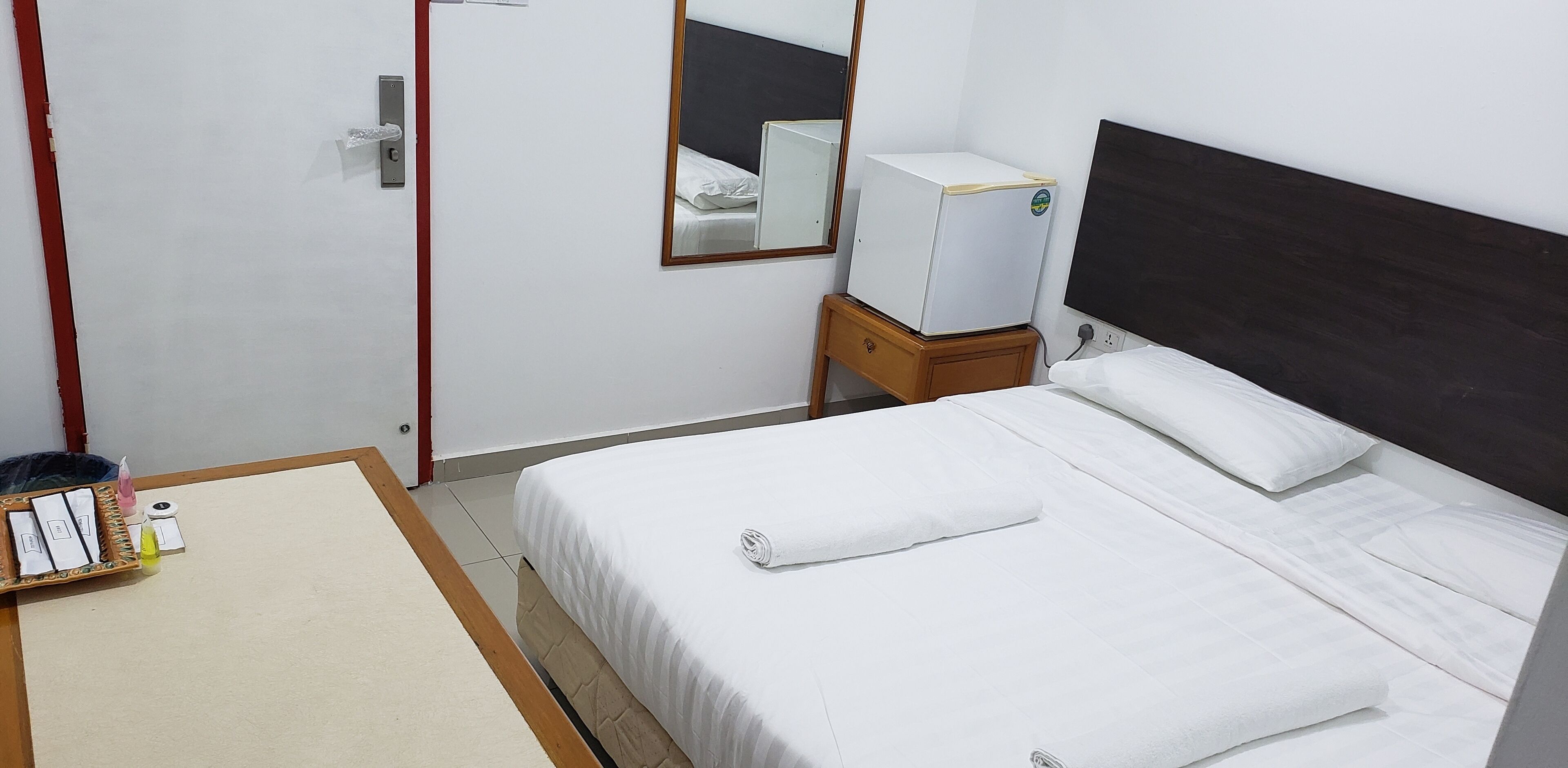 Ein Hotelzimmer mit einem Bett, einem Nachttisch, einem Spiegel, einem kleinen Kühlschrank und einer Tür.