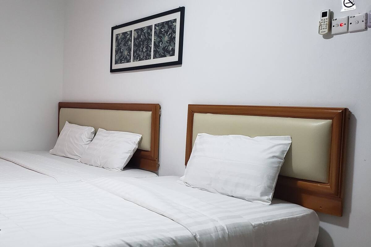 Una cama doble con sábanas blancas y cabecera de madera, un cuadro en la pared, y un teléfono y un interruptor de luz instalados en la pared.