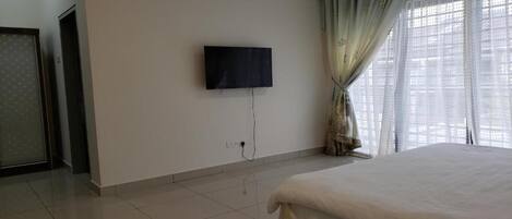 A hotel room with a bed, a television mounted on the wall, and a window with curtains.