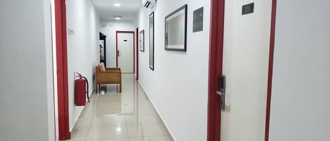 A hallway with white walls, red doors, and a fire extinguisher on the left.