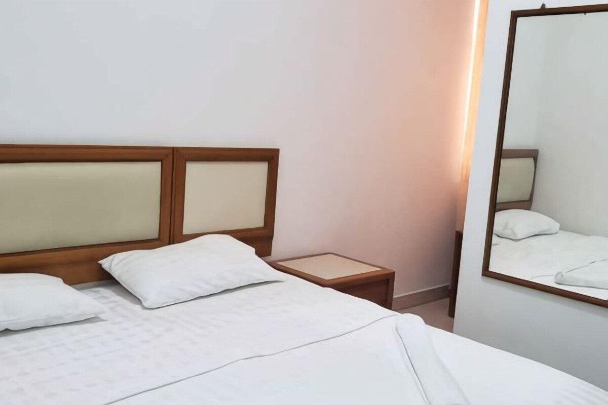 Une chambre d’hôtel avec un lit, une table de chevet, un miroir et une lampe fixée au mur.