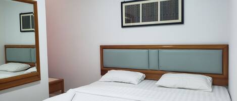 Un letto rifatto con cura, con una testiera in legno, due cuscini, un comodino e uno specchio appeso al muro.
