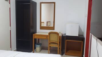 A hotel room with a bed, a desk with a chair, a mirror, a wardrobe, and a small trash bin.