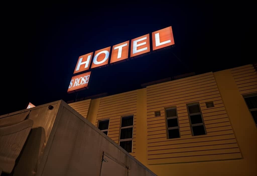 Segnaletica di un hotel con la scritta "HOTEL ROSES" illuminata su uno sfondo scuro.