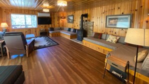 A cozy cabin interior with wooden walls, a fireplace, a sofa, and a television.