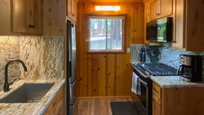 A compact kitchen with wooden cabinets, a stainless steel refrigerator, a microwave, and a sink with a marble countertop.