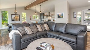 A modern living room with a sectional sofa, a coffee table with books and headphones, and a view of the kitchen and dining area. - Panoramic Paradise (Yosemite National Park)