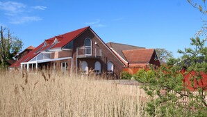 A two-story house with a red roof, a balcony on the second floor, and a brick exterior. - Ferienhaus mit drei Bädern in Dornumersiel (Dornumersiel)