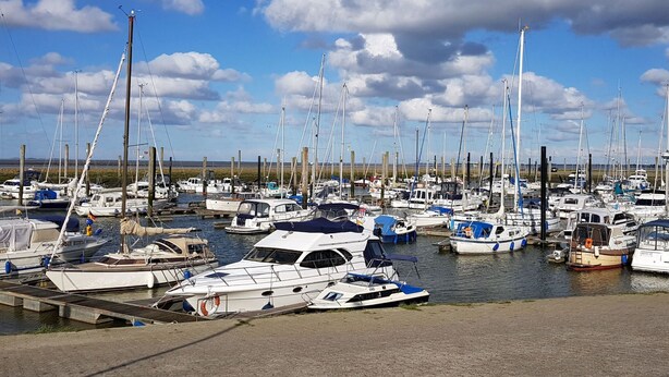 A marina with numerous boats docked at wooden piers under a partly cloudy sky. - Ferienhaus mit drei Bädern in Dornumersiel (Dornumersiel)