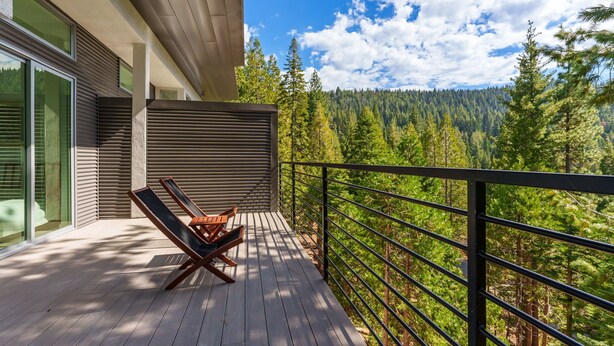 A wooden deck with two lounge chairs, a metal railing, and a view of a forested mountain range. - Apex Yosemite West (Yosemite National Park)