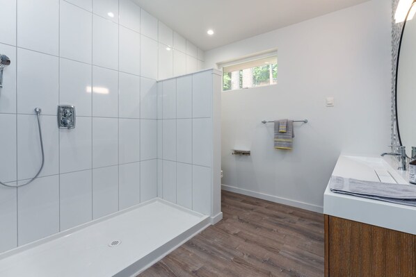 A modern bathroom with a shower, a window, and a wooden floor.