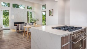 A modern kitchen with a marble island, stainless steel appliances, and large windows offering a view of greenery. - Apex Yosemite West (Yosemite National Park)