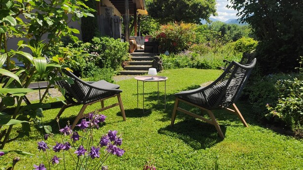 A garden with two wicker chairs, a small table, and a pathway leading to a building. - Vacation apartment Belchenblick  (Staufen im Breisgau)