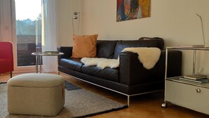 A modern living room with a black leather sofa, a red armchair, a small round table, and a glass cabinet. - Vacation apartment Belchenblick  (Staufen im Breisgau)