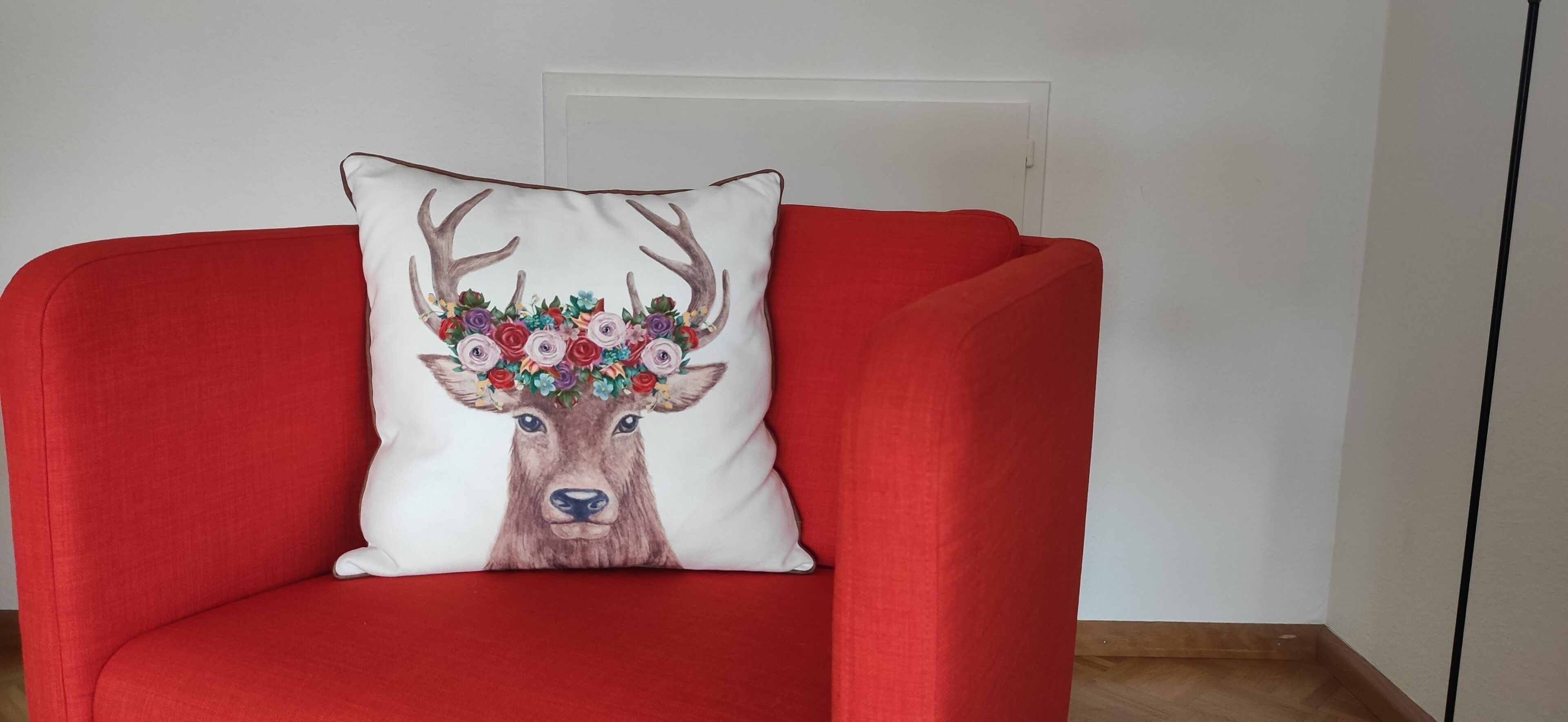 Un sillón rojo con un cojín blanco que muestra un diseño de ciervo y flores.