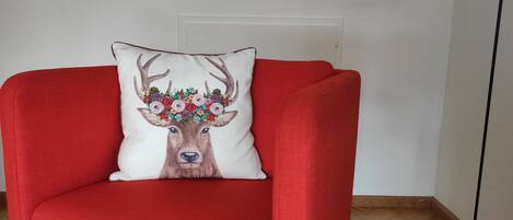 Un sillón rojo con un cojín blanco que muestra un diseño de ciervo y flores.