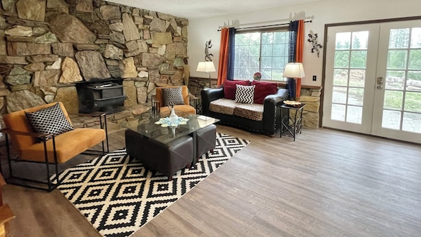 A living room with a stone wall, a fireplace, a sofa, a coffee table, and a ceiling fan. - Casa De Colores (Oakhurst)