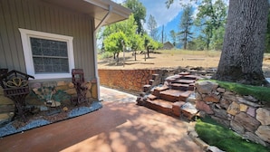 A house with a stone staircase leading to a porch, surrounded by trees and a clear sky. - Casa De Colores (Oakhurst)