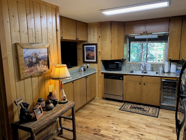 A wooden cabin-style kitchen with wooden cabinets, a granite countertop, a microwave, a dishwasher, and a window with a view of trees. - Chalet in the Pines (Fish Camp)