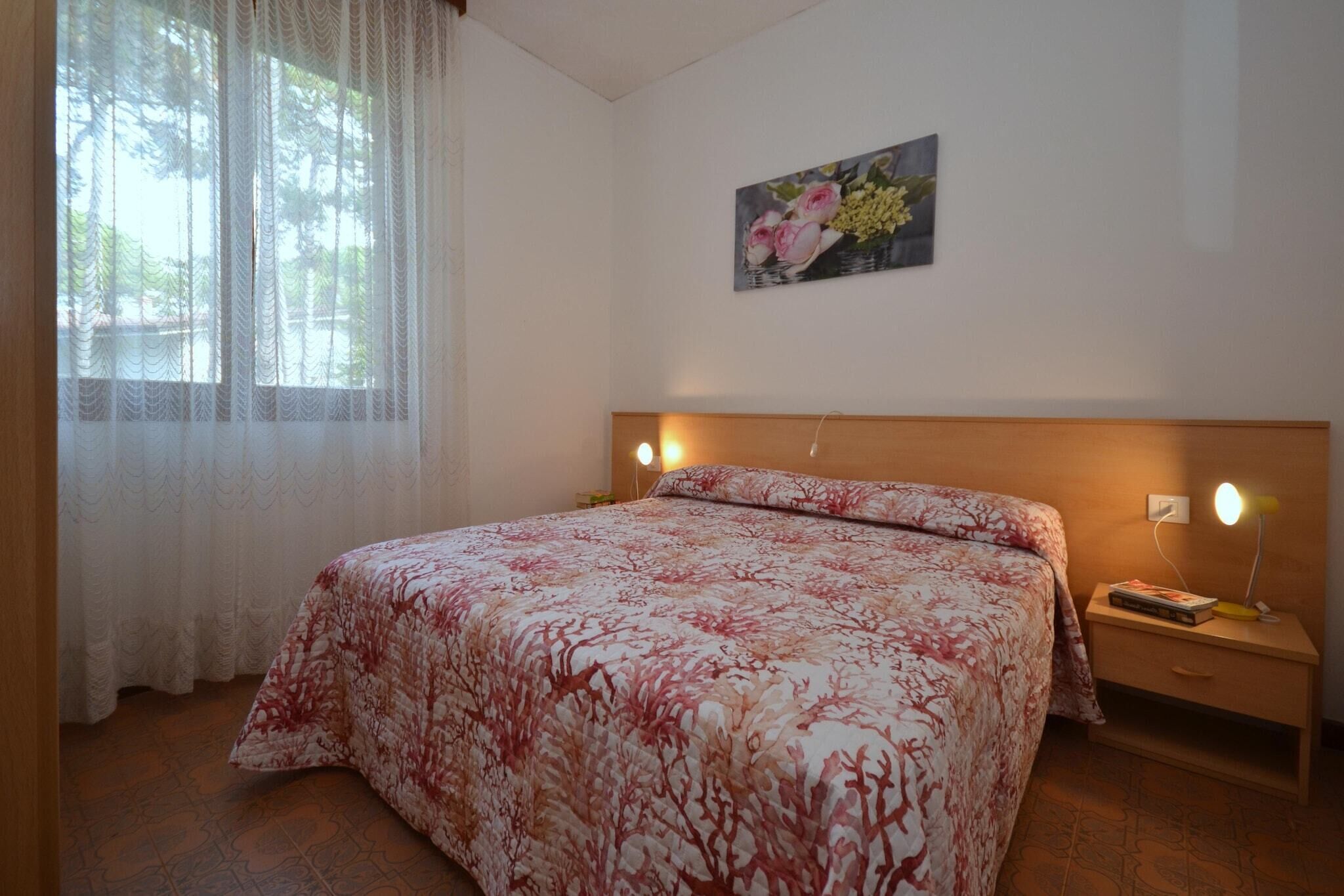 A bedroom with a bed, a nightstand, a lamp, a painting on the wall, and a window with curtains.