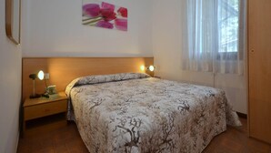 Een slaapkamer met een bed, nachtkastje, lamp, foto aan de muur en een raam met gordijnen.