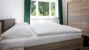 A bedroom with a bed, a window with curtains, a wardrobe, and a hanging light fixture. - Ferienhaus Yvonne in Wendorf im Bernstein Resort (Wendorf)