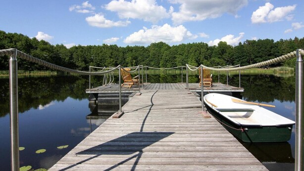 A wooden dock extending into calm water with a rowboat tied to it. - Ferienhaus Yvonne in Wendorf im Bernstein Resort (Wendorf)