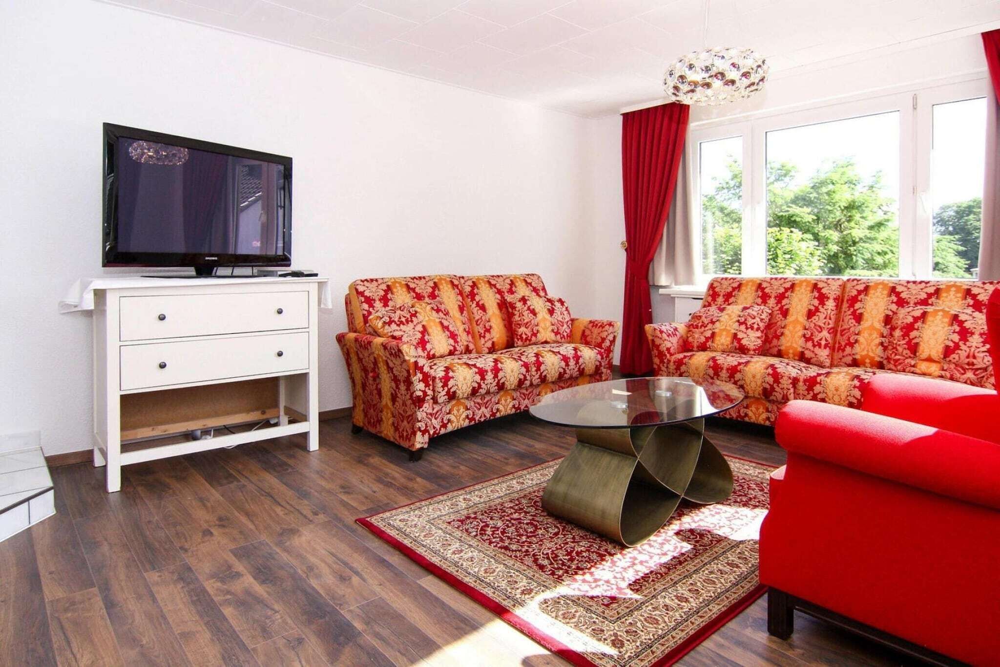 A living room with a TV, two sofas, a coffee table, and a window with curtains.