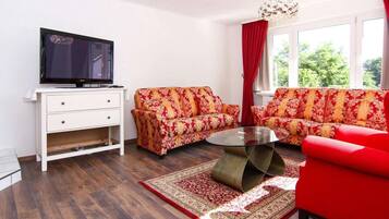 A living room with a TV, two sofas, a coffee table, and a window with curtains.