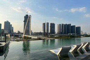 A modern bridge with a unique arch design spanning over a body of water, with a city skyline in the background. - The Opera Residence Luxury Vacation (Ho Chi Minh City)