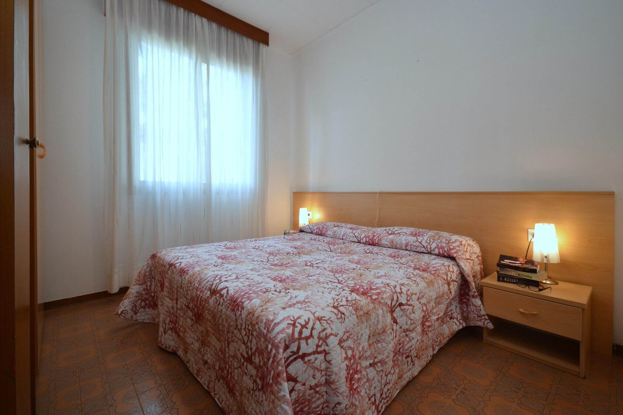Un dormitorio con una cama, un mesita de noche, una lámpara y una ventana con cortinas.