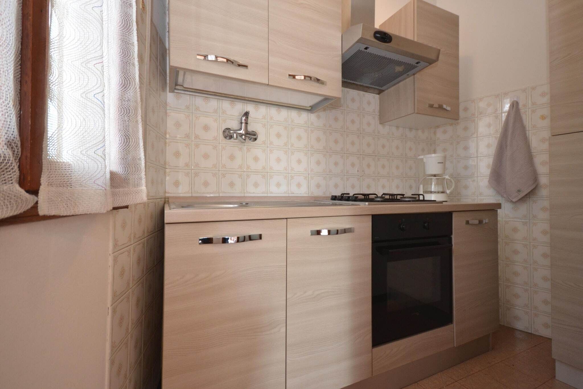 Una cocina con armarios de madera clara, un horno negro y una cafetera en la encimera.