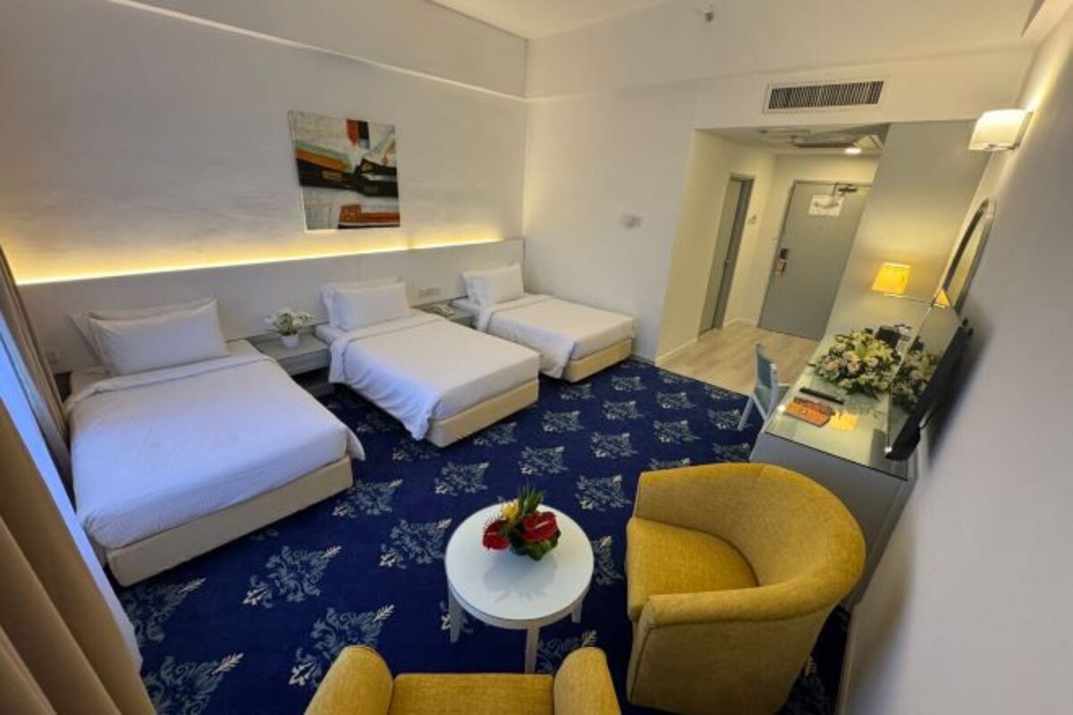 A hotel room with two beds, a small table with flowers, and a yellow armchair.