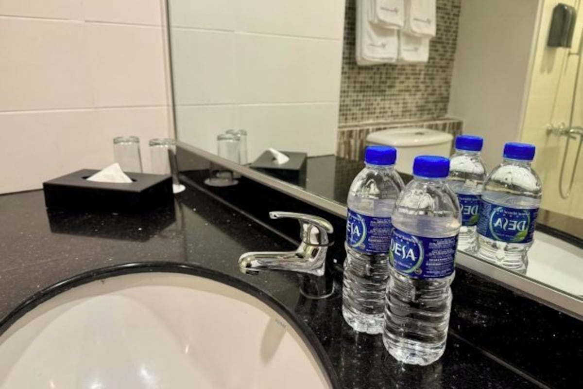 A bathroom sink with a mirror, a faucet, and several water bottles labeled 'DESA' on a black countertop.